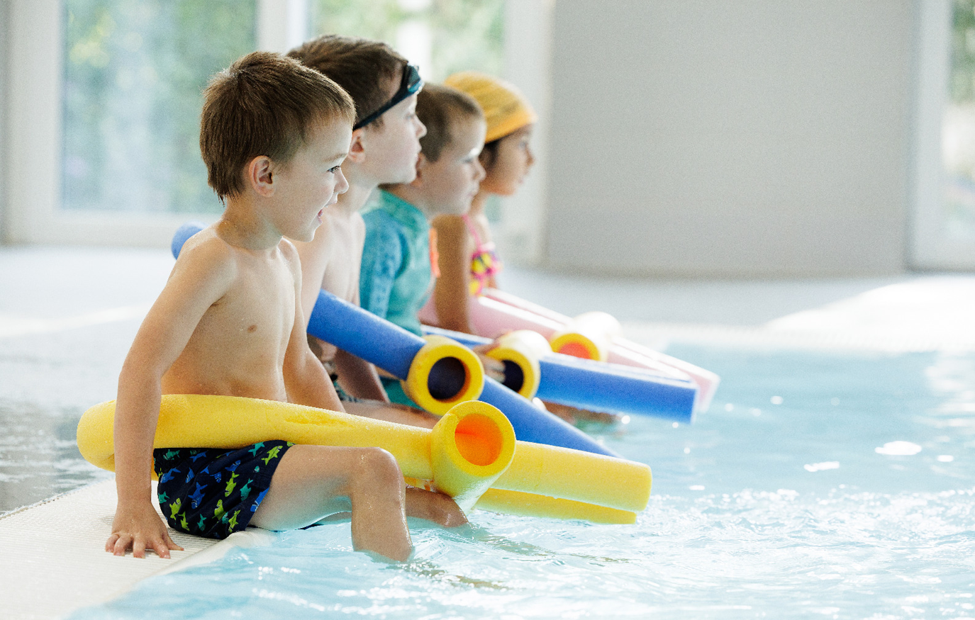 Ein EInblick in den Schwimmkurs mit lachenden Kindern am Beckenrand