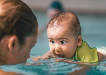 Babyschwimmen Mama und Baby im Wasser- beide schauen sich an, das Baby hält den Mund weit geöffnet.
