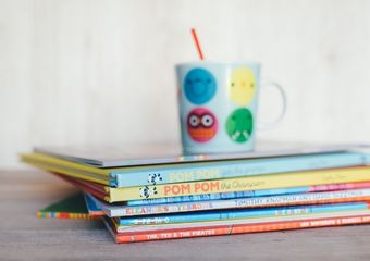 Kinderbücher liegen gestapelt auf einem Tisch - darauf steht eine Kindertasse