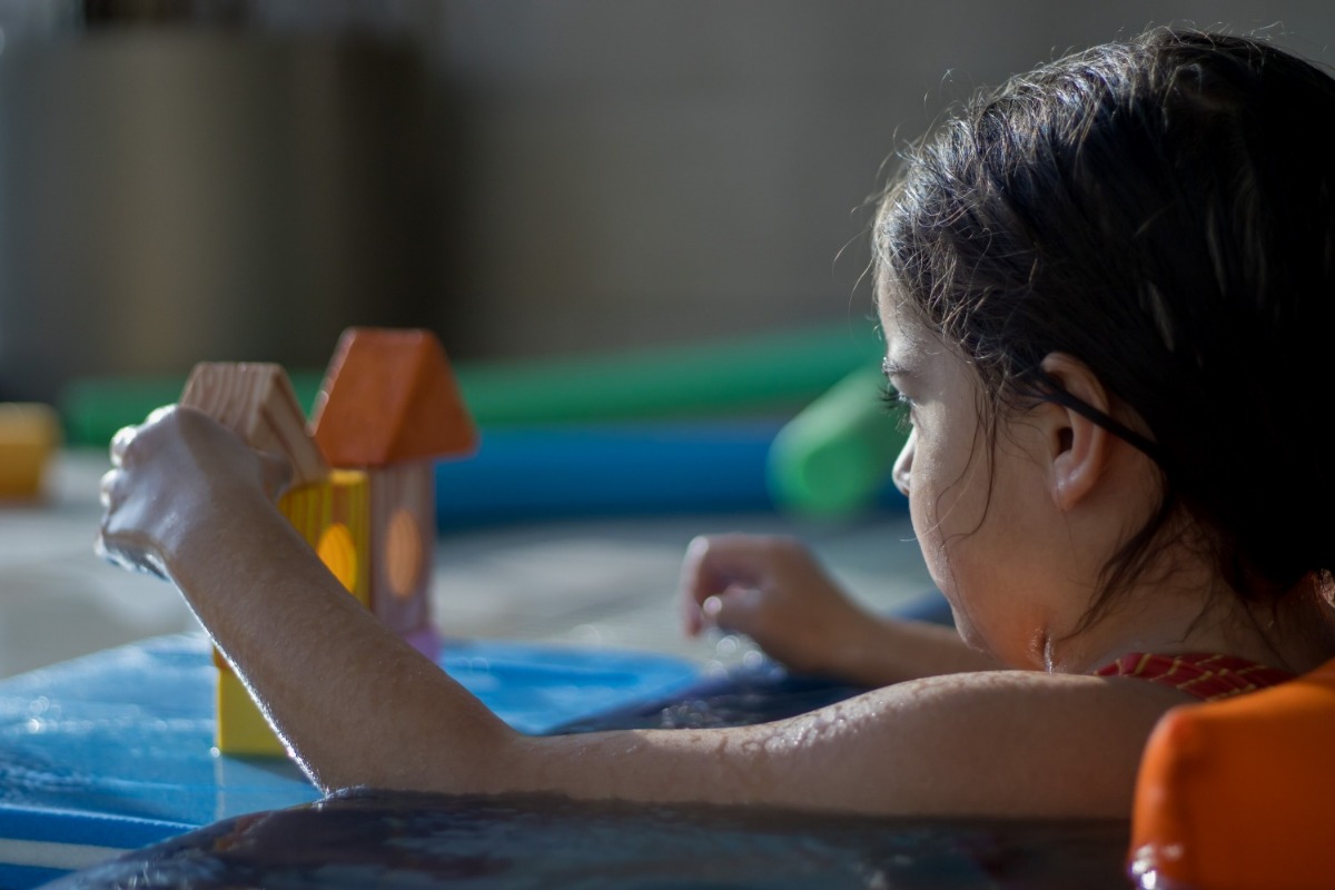 Badewannenwasser mit Schaum und Spielzeugen, von dem Baby sieht man nur die Hände, dieses spielt mit viele bunten Wassertierchen.