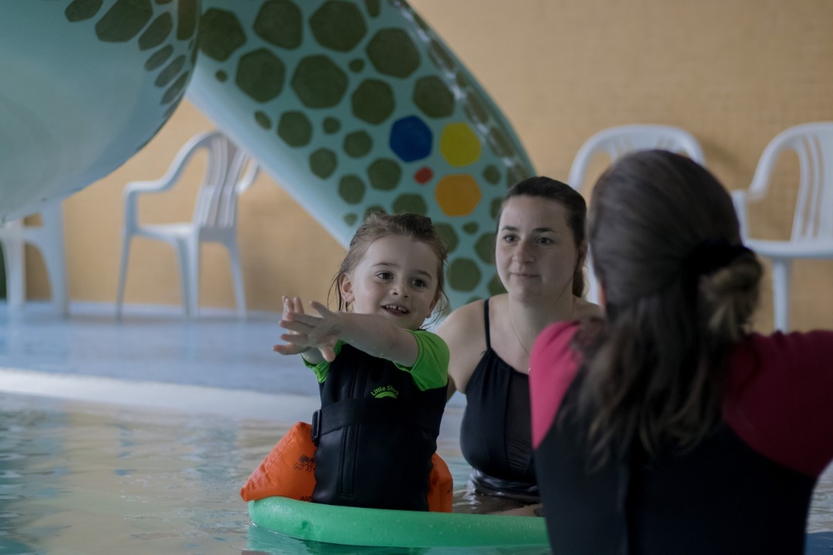 Ein Mädchen übt mit der Kursleiterin die Pfeilarme, Mama im Hintergrund