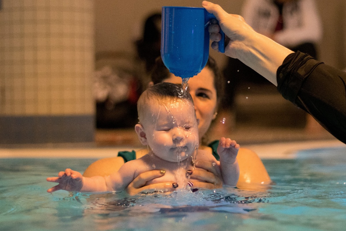 Mama und Baby im Wasser- beide schauen sich an, das Baby hält den Mund weit geöffnet.