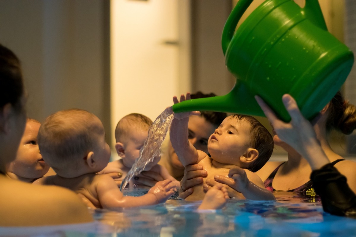 Ein Mutter und ihr Baby sind in einem Schwimmbecken. Die Mutter schaut der Kleinen ins Gesicht, während das Baby lächelt.