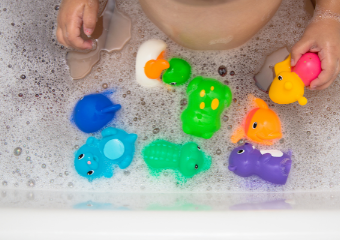    Badewannenwasser mit Schaum und Spielzeugen, von dem Baby sieht man nur die Hände 