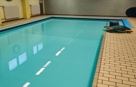 Links das Schwimmbecken der Kirschenfeldschule, rechts der Beckenrand, auf diesem liegen bunte Schwimmnudeln für den Unterricht
