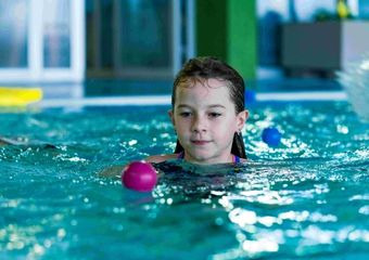 Ein Mutter und ihr Baby sind in einem Schwimmbecken. Die Mutter schaut der Kleinen ins Gesicht, während das Baby lächelt.