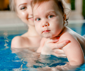 ein Kleinkind ist im Haltegriff der Mama beim Babyschwimmen
