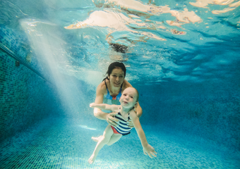 Eine Mama und ihr Kind sind beide unter Wasser, die Mutter ist hinter dem Kind und hält es im Arm fest.