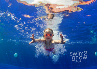 Ein kleines Mädchen mit pinker Schwimmbrille,  das unter Wasser taucht und schwimmt.