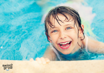 das Gesicht eines Jungen, das in die Kamera blickt, der Junge hält sich am Beckenrand eines Schwimmbeckens fest.