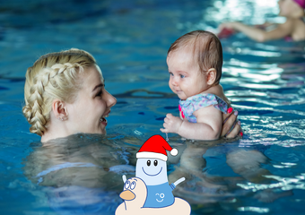 Eine Mutter mit blonden, geflochtenen Haaren, hält ihr Baby im Wasser in den Händen, beide schauen sich an. Im Vordergrund ist Bobo Boje abgebildet in einem Schwimmring.