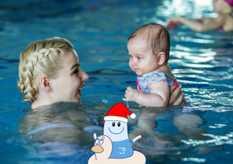 Warum ein Schwimmkurs das perfekte Weihnachtsgeschenk ist Eine Mutter mit blonden, geflochtenen Haaren, hält ihr Baby im Wasser in den Händen, beide schauen sich an. Im Vordergrund ist Bobo Boje abgebildet in einem Schwimmring.